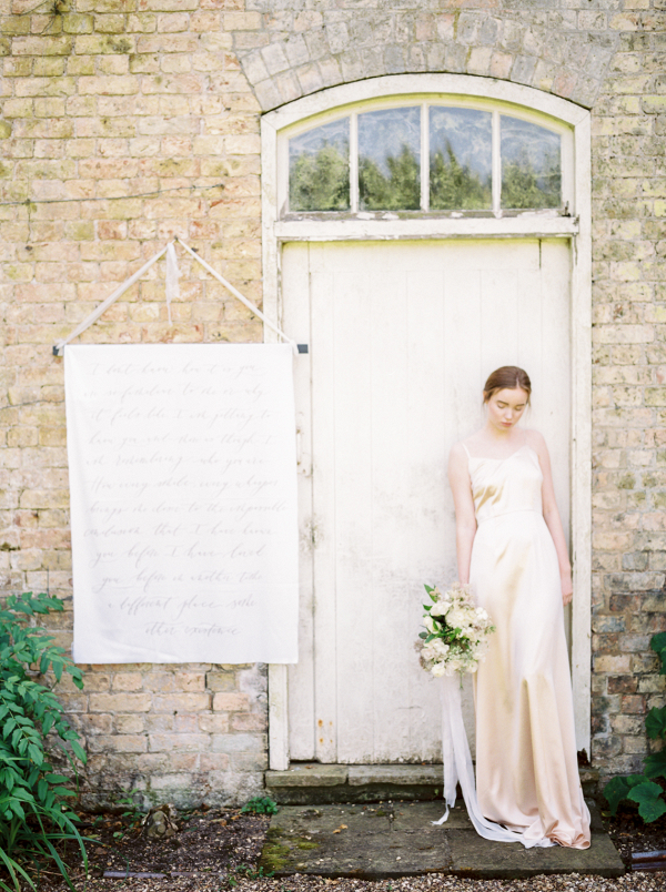fine art bride wearing golden silk wedding gown leaning against an old wooden door