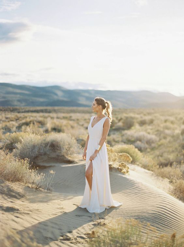 modern bride wearing sleek white wedding dress with statement gold cuff bracelet stood in the sand