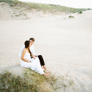 sitting in the sand dunes on the beach of their engagement shoot