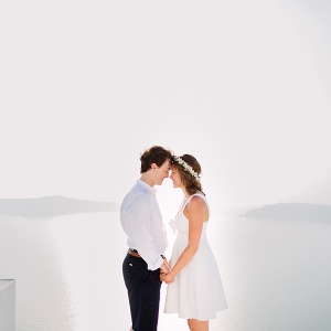 couple stand together with the background of the ocean surrounding  Santorini 