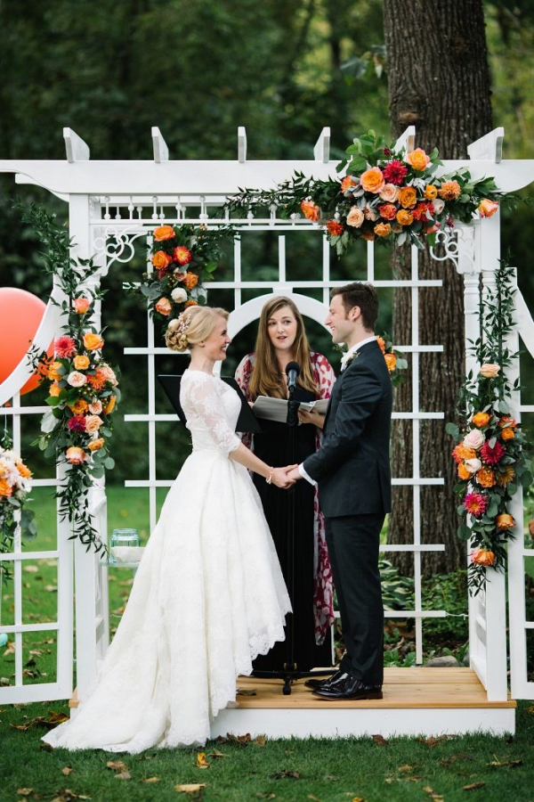 Outdoor wedding ceremony with orange floral arbor
