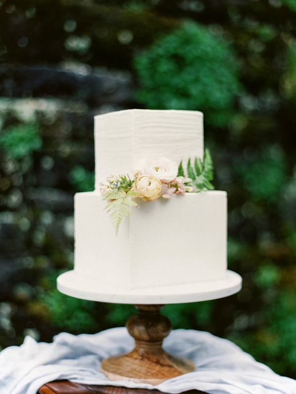 Ivory square wedding cake on a simple wooden cake stand