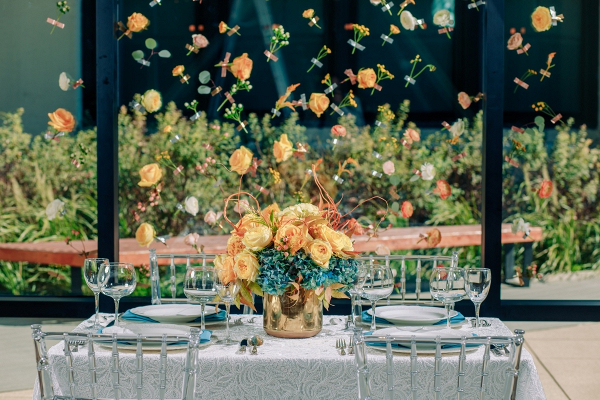 Orange and teal wedding tablescape with flower backdrop