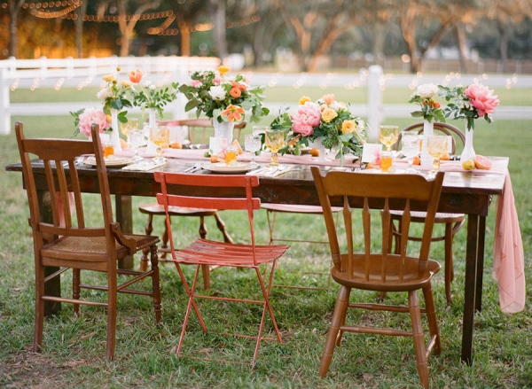 Outdoor Wedding Reception Decor with Vintage, Mis-Matched Wooden Chairs and Orange, Yellow and Pink Wedding Centerpieces with Cafe Lighting