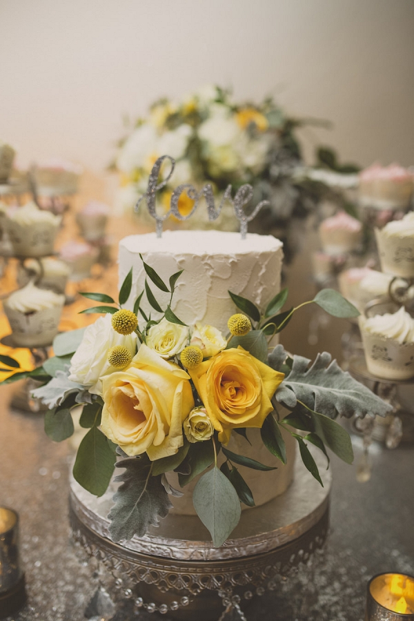Two Tier Round White Wedding Cake with Yellow Roses and Greenery on Silver Cake Stand with Love Cake Toppe