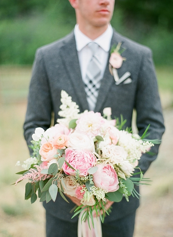 Groom in a gray suit holds a pink and white wedding bouquet