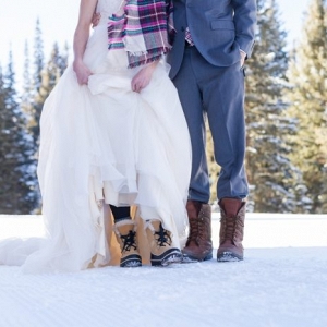 Bride and groom standing on the snow in their bridal attire and snow boots