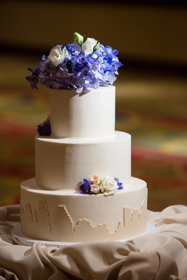 Elegant 3-tier wedding cake with floral topper and fondant cityscape