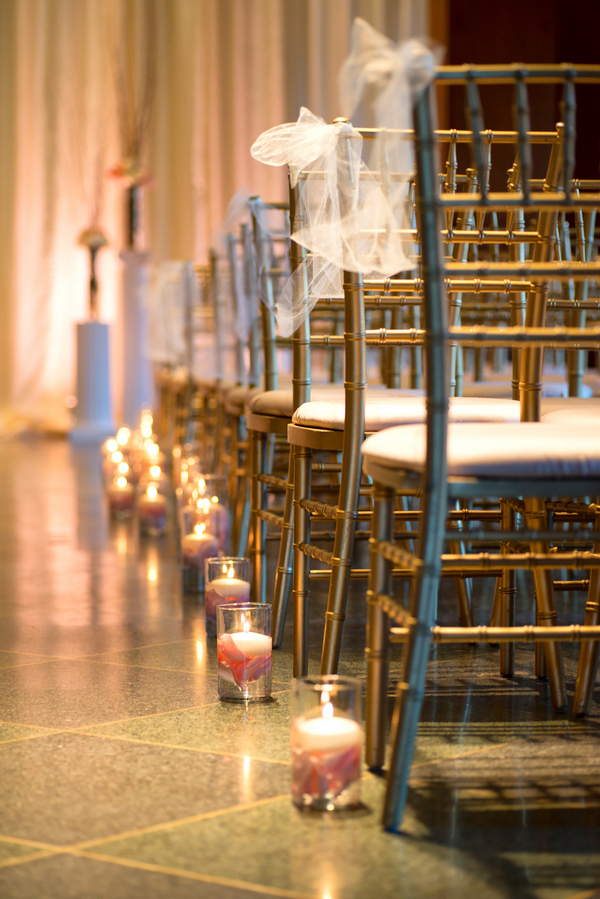 Adorably decorated chiavari chairs with tulle ribbon and a floating candle and flower petal lined aisle