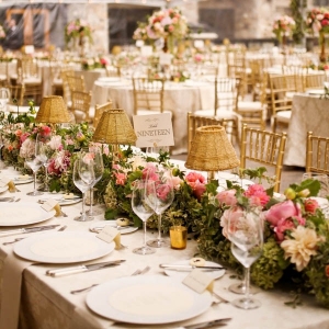 Romantic tented wedding tablescape with a lush floral table runner, gold lamps, and chiavari chairs