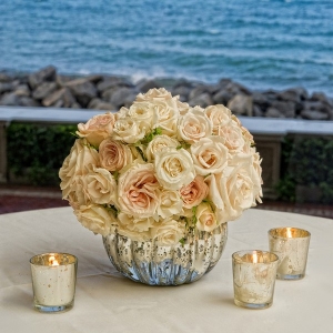 Elegant cream and white rose centerpiece in a mercury glass vase surrounded by mercury glass candles