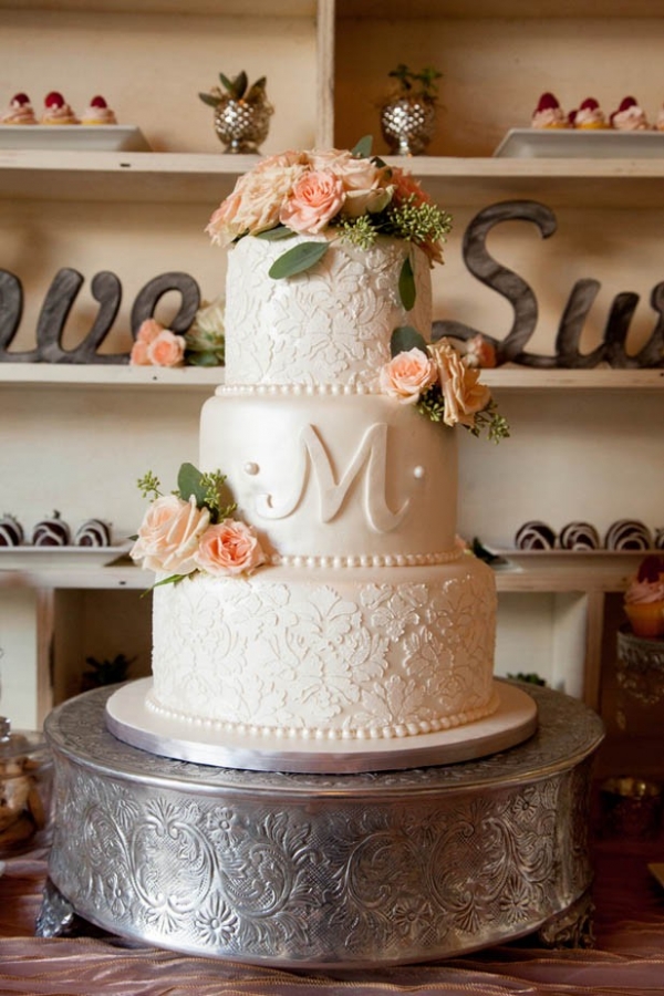 Beautiful lace textured wedding cake with monogram and rose accents on silver stand