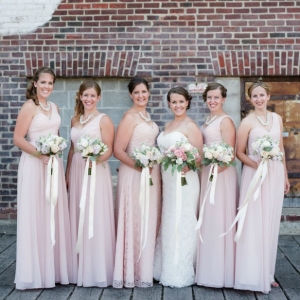 Floor length, one shoulder bridesmaid dresses in pink with garden inspired bouquets tied with ribbon