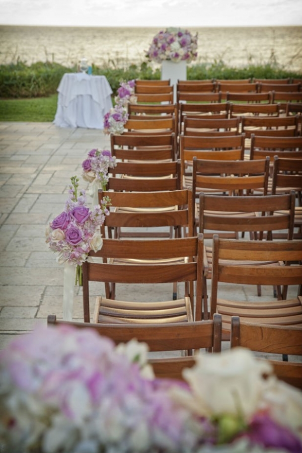 Elegant wedding ceremony overlooking the ocean with wooden chairs and rose bouquet aisle markers