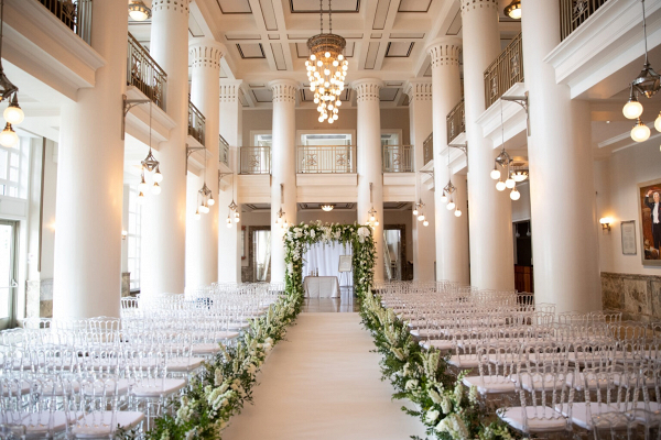 Elegant indoor wedding ceremony with greenery filled aisle and arch