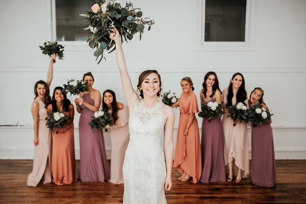 Bride holding bouquet in front of bridesmaids wearing miss matched dresses