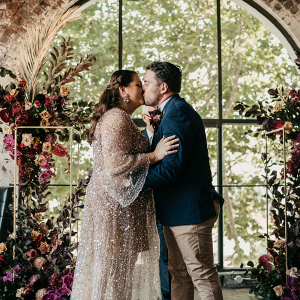 Boho modern wedding ceremony with lush floral backdrop and sparkle wedding dress