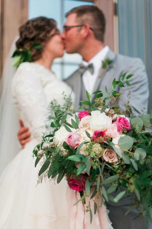 Gorgeous portrait of a bride and groom, kissing behind her amazing bouquet!