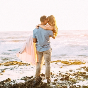 Guy holding girl on a rocky beach.