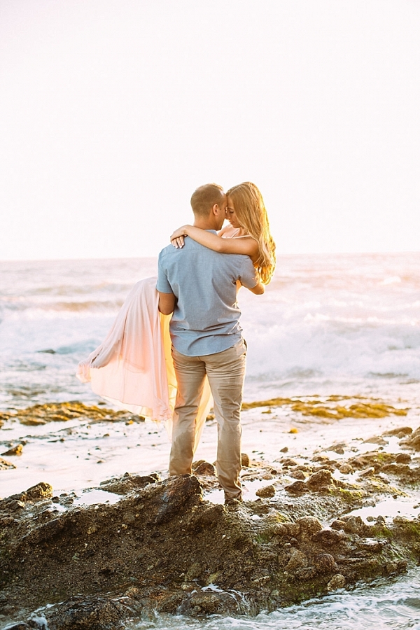 Guy holding girl on a rocky beach.