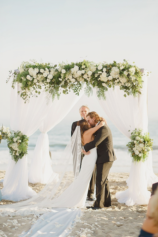 Beach wedding ceremony with draping and floral arch