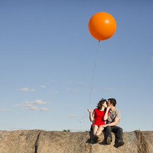 Couple sitting atop a hay bale and holding a giant red balloon