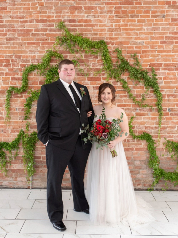 Bride and groom with greenery wedding ceremony backdrop